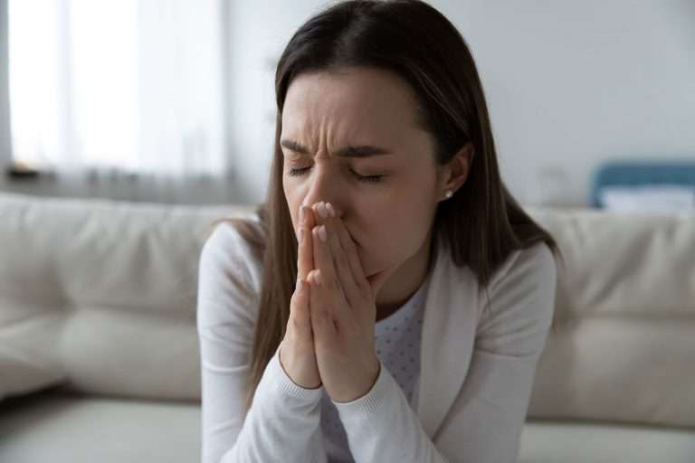 Woman sitting on couch, holding face in hands