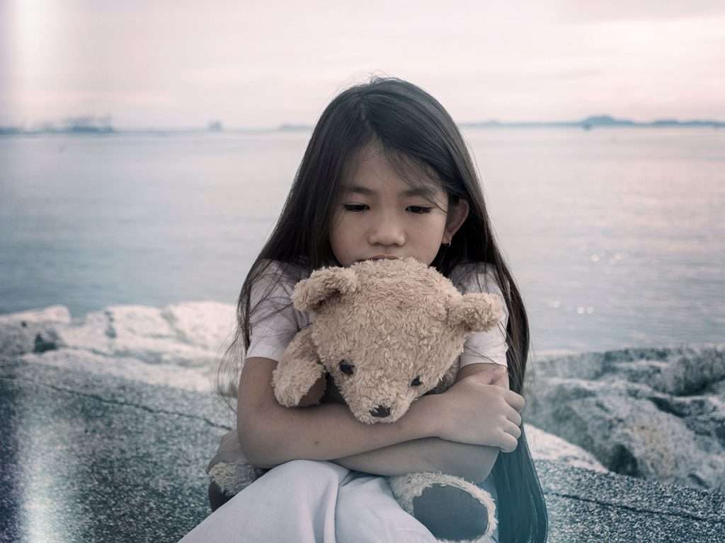 Young girl sitting on rocky shore, holding a teddy bear