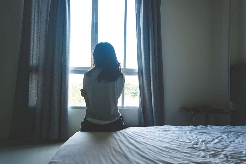 woman sitting on bed in room with light from window