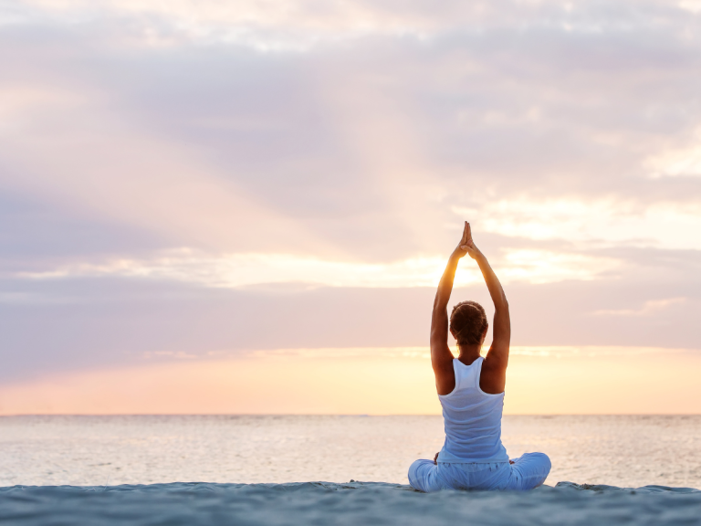 Woman doing yoga on the west palm beach in the sunset preparing for a cancer survivor therapy session.